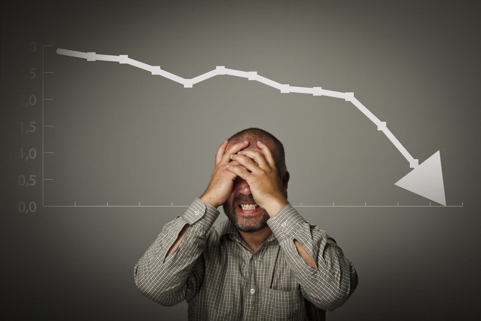 A man holding his head in front of a line graph.